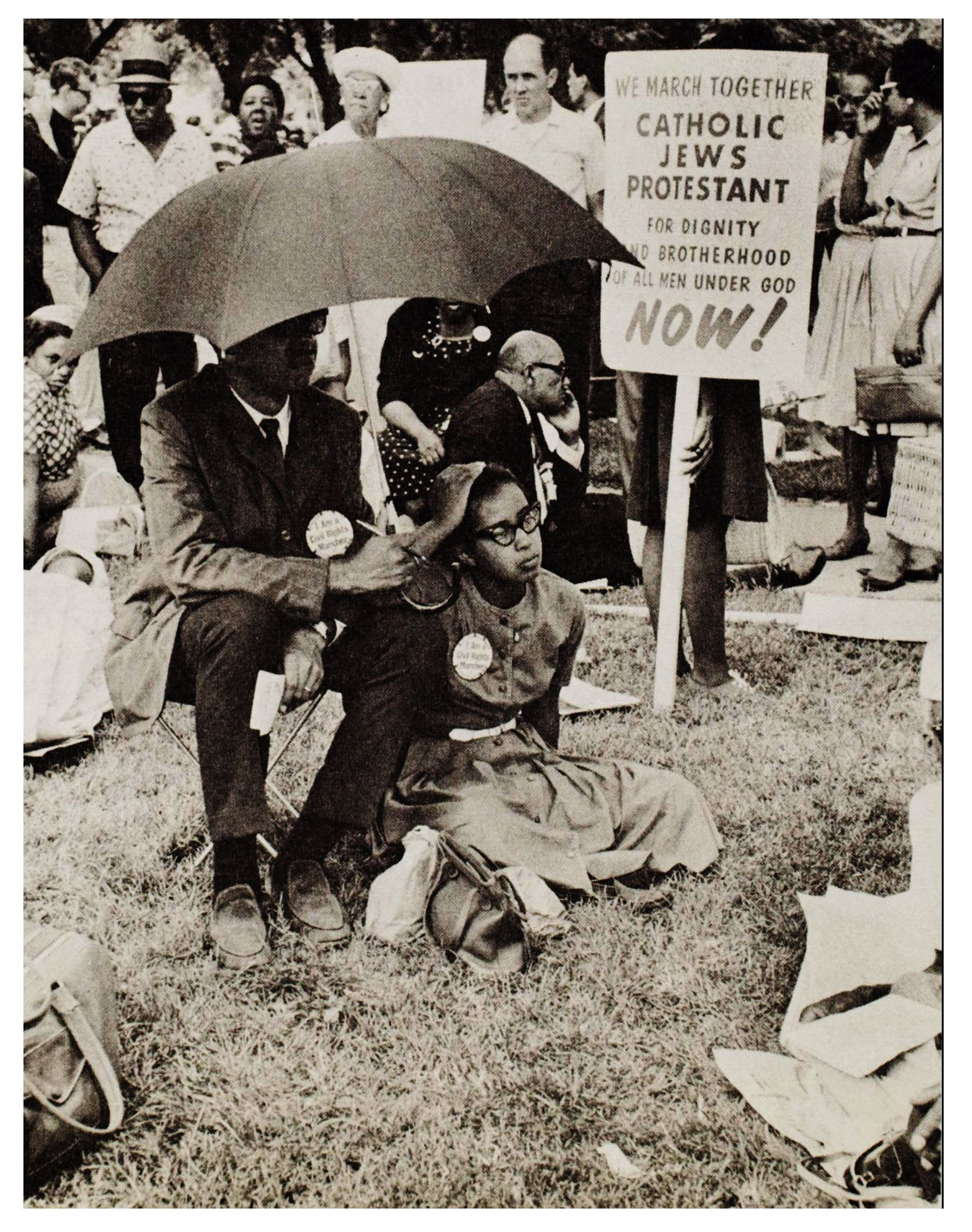 Black and white protestors sitting and standing with a sign that says 'We march together, Catholic Jews Protestants'.